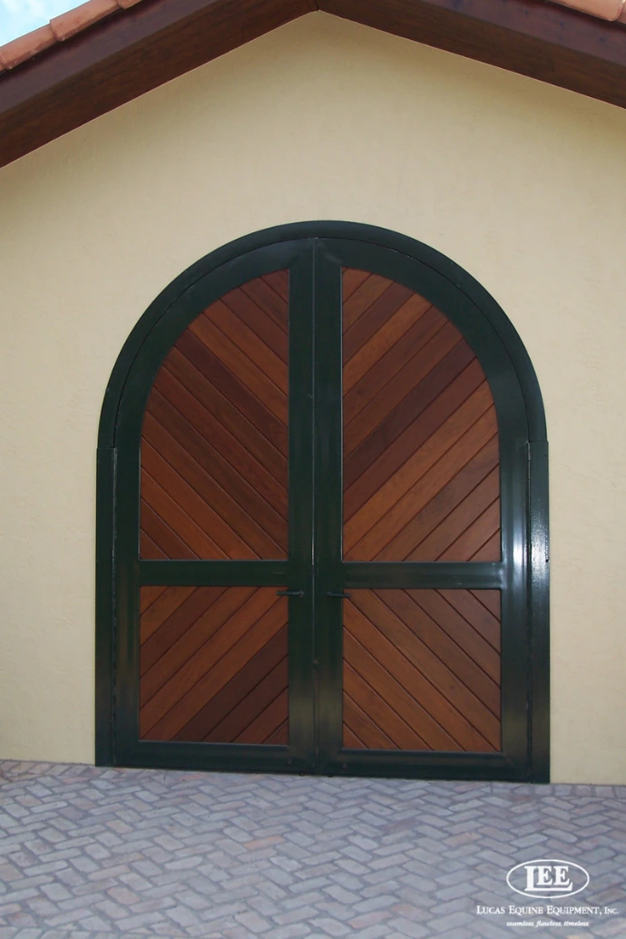 Close-up of arched double door with dark green metal frame and diagonal wood plank panels
