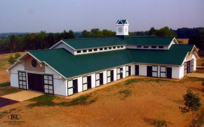 Large white barn complex with green metal roof and multiple stall openings