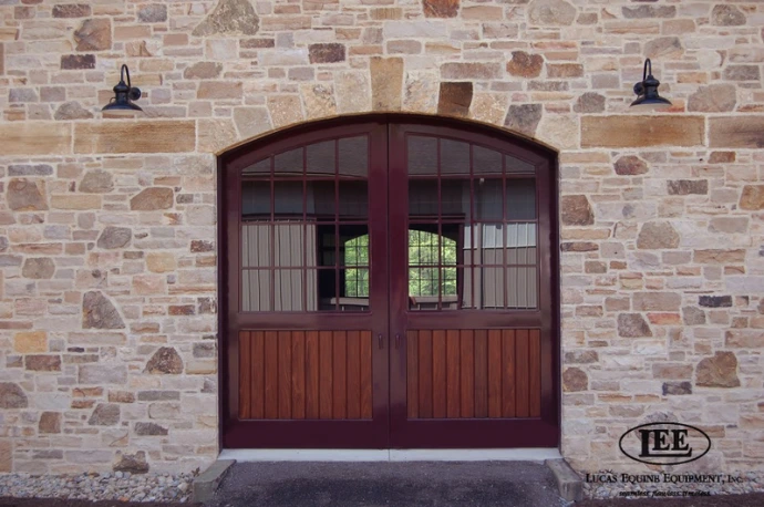 Stone facade barn with arched mahogany double doors featuring grid window pattern