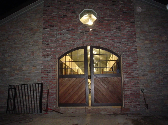 Night view of barn with illuminated arched doorway featuring wood and glass panel doors