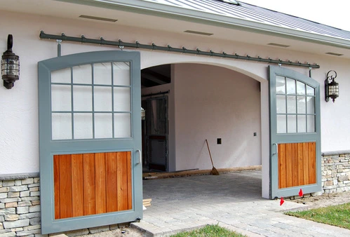 Gray metal double doors with upper glass panels and wood lower sections under arched opening