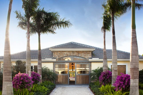 Tropical setting barn entrance with wood doors between palm trees and flowering plants