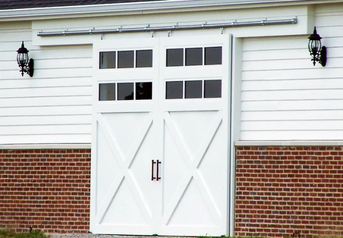 White barn with carriage-style doors featuring X-pattern and multi-pane windows between brick accents