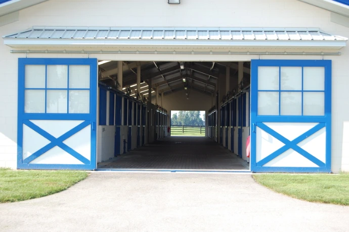 Bright blue barn exterior with white trim and X-pattern stall doors flanking central opening