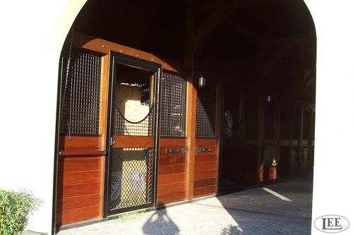 Mahogany sliding stall door with wire mesh upper panel and decorative horseshoe detail open to exterior