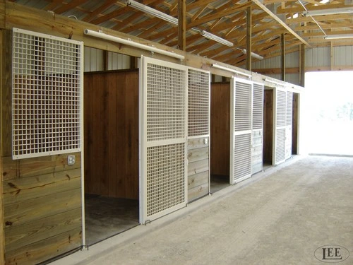 Modern barn aisle with white-framed stalls featuring wire mesh panels and natural wood accents