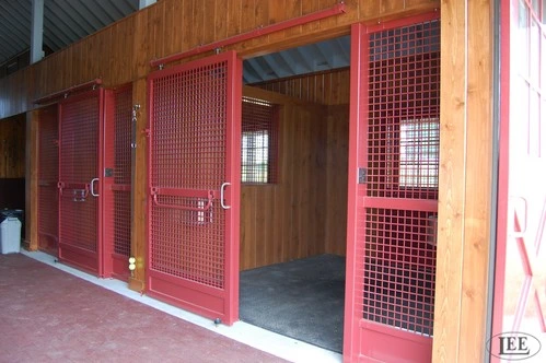 Red metal stall doors with wire mesh panels along covered barn aisle with concrete floor