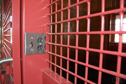 Detail of red painted metal grid mesh stall door panel with hardware visible