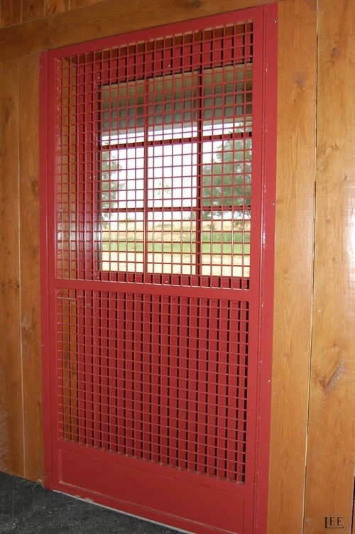 Close-up of red metal stall door with grid wire mesh panel and solid lower section