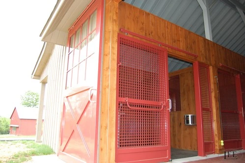 Red metal sliding stall door with wire mesh panel open to exterior barn view