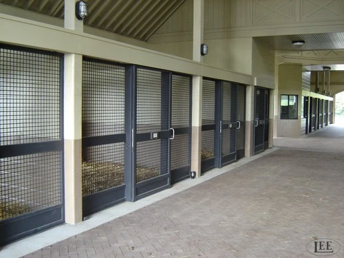 Sage green and gray stall fronts with wire mesh sliding doors along barn corridor