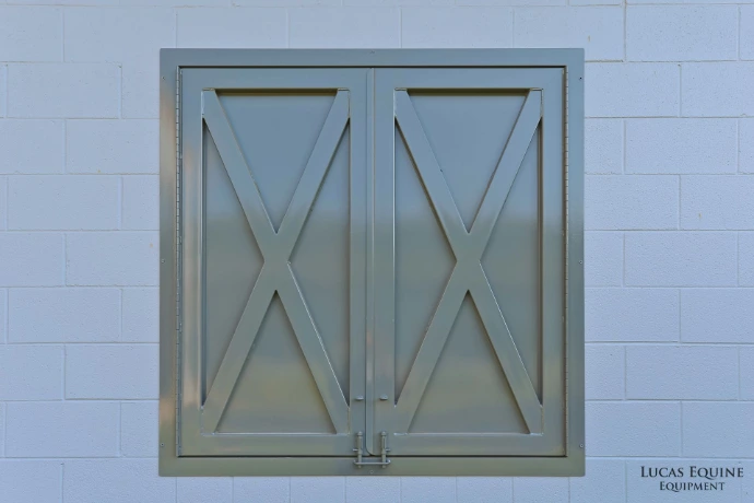 Sage gray painted window with diagonal X-brace pattern on pale blue barn wall