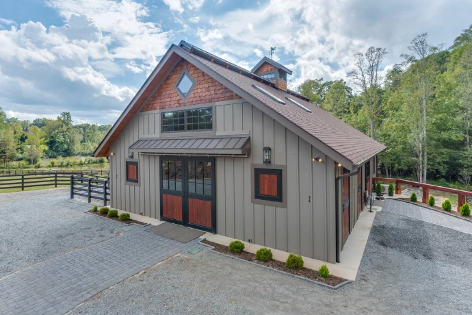 Gray wood barn building with mix of window styles and diamond detail in gable