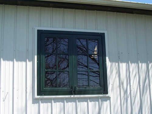 Forest green double casement window with decorative tree branch overlay pattern on white barn