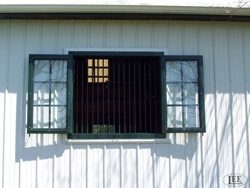 Green painted window with black vertical security bars flanked by small six-pane windows