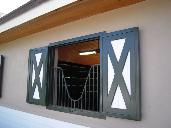 Gray painted window with X-pattern decorative shutters open showing interior barn view