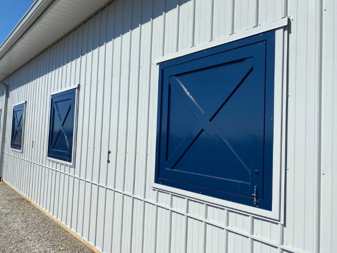 Blue painted barn sliding door with X-pattern design on white vertical siding exterior