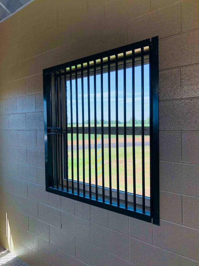 Black vertical bar window on gray concrete block wall overlooking green pasture