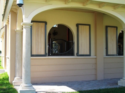 Cream colored covered area with three arched windows featuring black metal grills