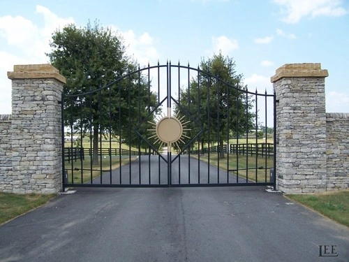 Black metal double gates with circular sun medallions between stacked stone pillars with decorative caps
