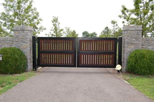 Brown wood double gates with vertical slat design centered between stone pillars with manicured shrubs