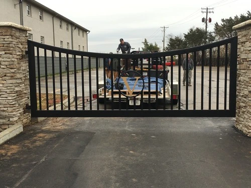 Black vertical bar gate being installed by workers on asphalt driveway