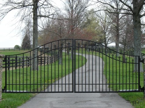 Black metal double gates with decorative curved top design spanning asphalt driveway