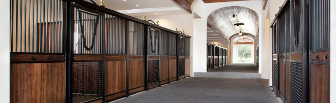 Covered barn aisle with mahogany stall fronts, natural wood lower panels and barrel vaulted white ceiling with arched window