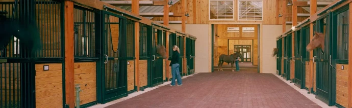 Forest green stall fronts with natural pine lower panels, person walking down aisle in timber-frame barn with pink flooring
