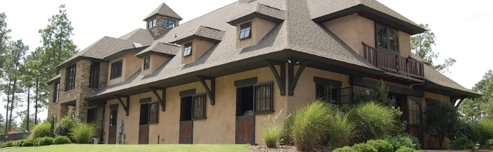 Craftsman-style barn exterior with timber-frame details, dormer windows, dark shutters and professional landscaping