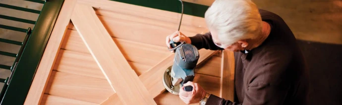 Person using electric router tool on natural wood board edge for precision woodworking