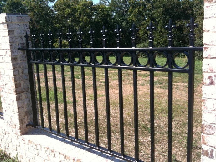 Black metal vertical bar railing mounted on aged stone pillars with green pasture beyond