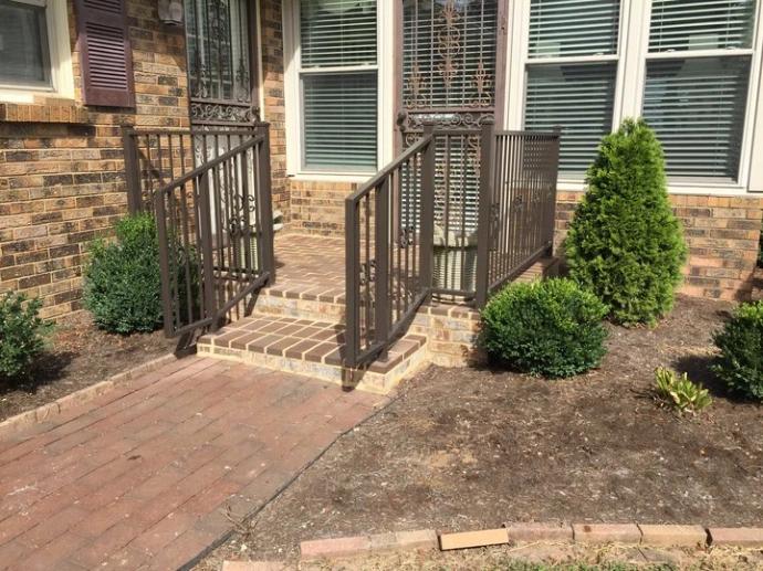 Brown or bronze powder-coated vertical bar deck railing on residential brick home exterior with stairs and landscaping