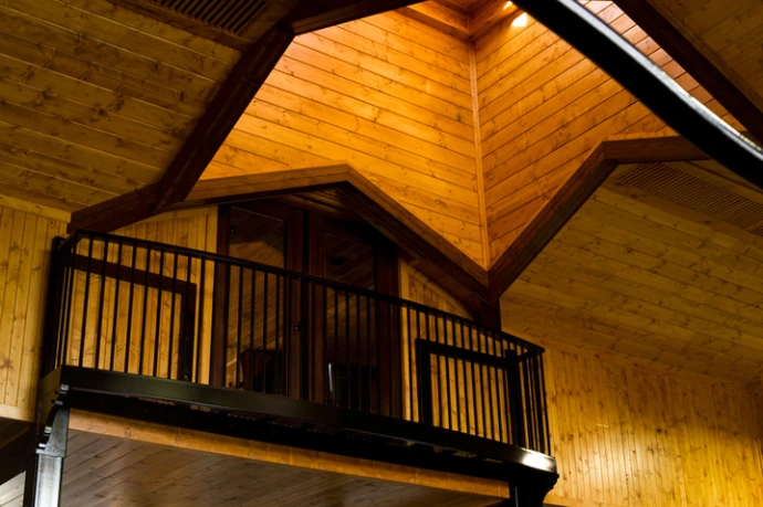 Interior view of black metal vertical bar railing on upper level balcony under vaulted natural wood plank ceiling
