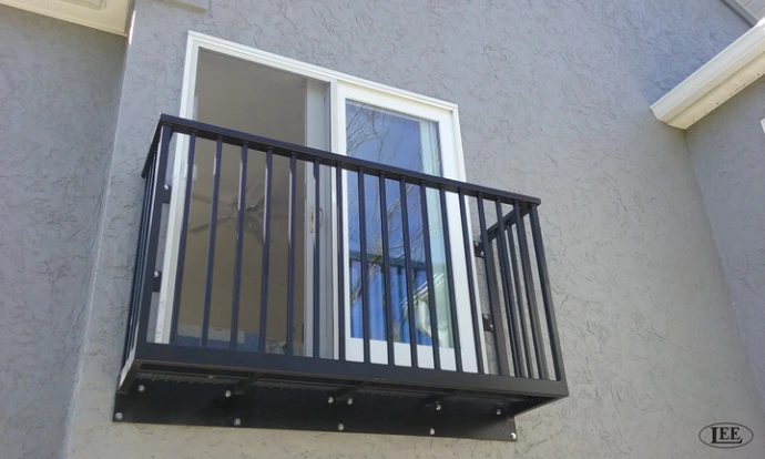 Black metal vertical bar railing on small exterior balcony of gray stucco building with white trim window