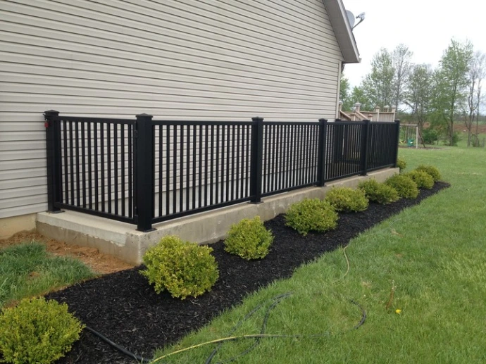 Black aluminum vertical picket railing panels mounted on concrete retaining wall along residential home exterior with green lawn and manicured shrubs