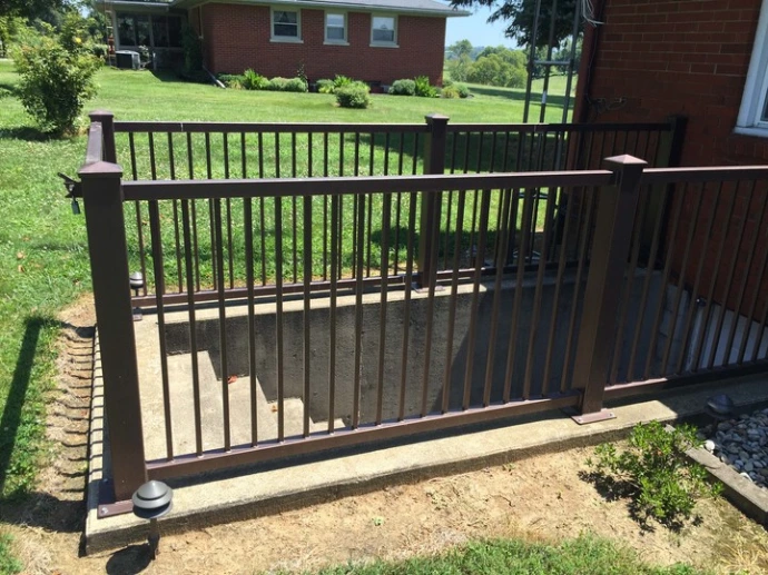 Black aluminum vertical picket railing installed on residential deck with steps overlooking green lawn with mature trees