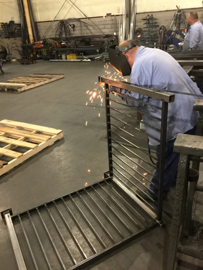 Black horizontal slat railing panels being powder coated or painted in industrial manufacturing facility