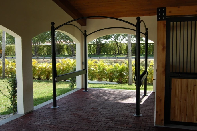 Black metal arched stall entrance with natural wood door and decorative upper grill opening to green lawn beyond