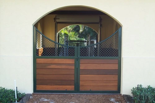 Dark green double doors with horizontal mahogany wood panels set in arched cream stucco wall opening