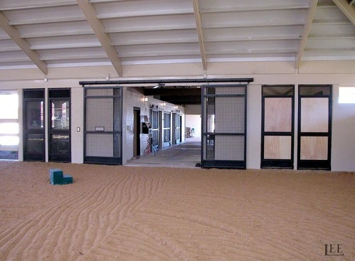 Interior covered barn aisle showing black metal framed stall fronts and sliding door openings with paved floor