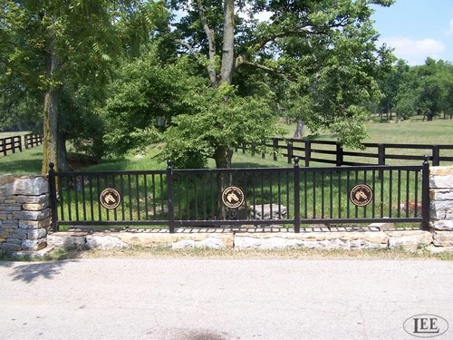 Black aluminum fence panels with circular horse medallion decorative inserts on stone wall with pasture beyond
