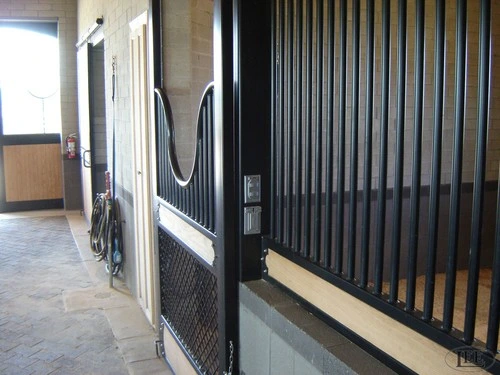 Modern barn aisle with tall black metal vertical bar partition walls and white horse visible in stall