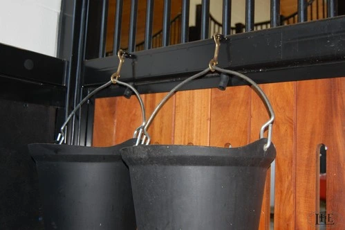 Black curved metal yoke or bracket with chain suspension hardware hanging from black stall front