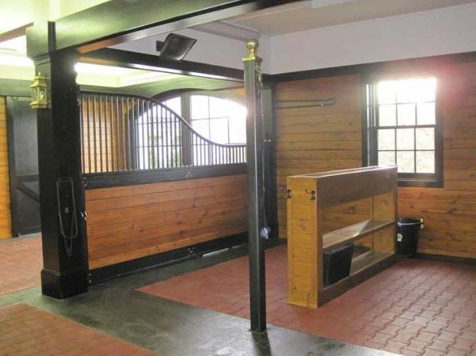 Black metal sliding stall door open revealing interior with natural wood walls and brick paver flooring