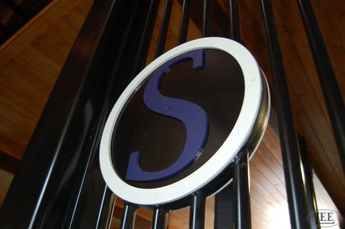 Close-up of circular metal medallion plaque with letter "S" in blue and white on black metal stall front