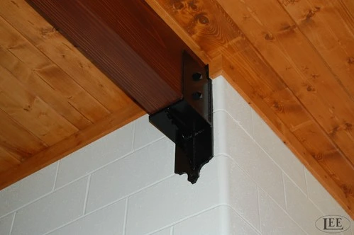 Black metal hinge hardware or mounting bracket on white wall under natural wood plank ceiling