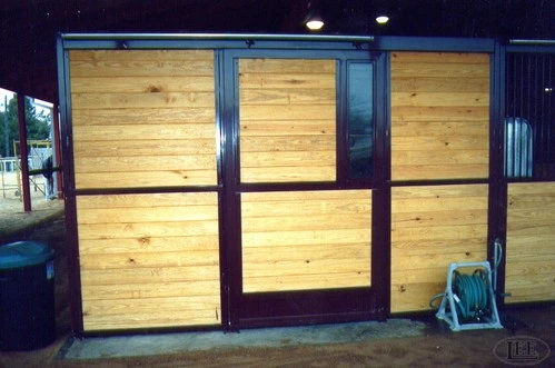 Evening exterior view showing burgundy painted stall fronts with natural pine panels and illuminated interiors in covered barn