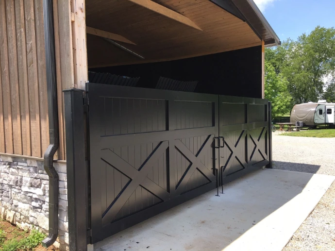 Modern barn exterior with large dark gray metal sliding doors featuring X-pattern design on horizontal wood siding