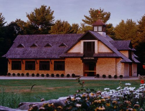 Timber-frame barn under construction with exposed wood trusses, multiple gables and earth-tone finish